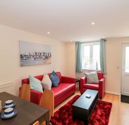 A living room with red sofa and armchair a black coffee table and dining table with cups at Mellstock in Nottington near Weymouth