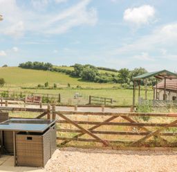 A wooden fenced patio area with garden furniture and a view of green fields and a hill at Emminster in Nottington near Weymouth