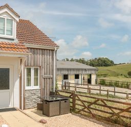 A house with a tiled roof and a small patio area with furniture next to a fenced rural farmland at Emminster in Nottington near Weymouth