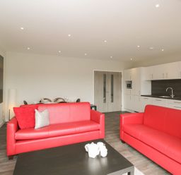 A living room with two red sofas and a black coffee table near a kitchen with white cabinets at Egdon Heath in Nottington near Weymouth