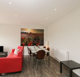 A living room with a red sofa dining table with six chairs and a large flower field photo on the wall at Egdon Heath in Nottington near Weymouth