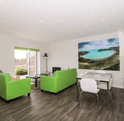 A living room with green sofas a coffee table a dining table with white chairs and a large landscape photograph on the wall at Overcombe Mill in Nottington near Weymouth