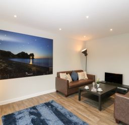 A living room with two brown sofas a black coffee table a floor lamp and a large wall photograph at Dirdale in Weymouth