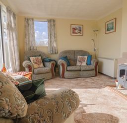 A sitting room with patterned sofas, a wood burning stove, curtains and framed pictures at Broadstones in Bridport