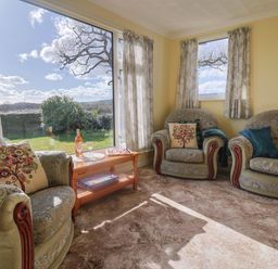 A living room with upholstered armchairs and a sofa around a wooden coffee table with a bottle and glasses at Broadstones in Bridport