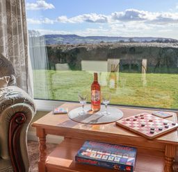 A wooden coffee table with a wine bottle glasses and a board game next to a patterned armchair and window at Broadstones in Bridport