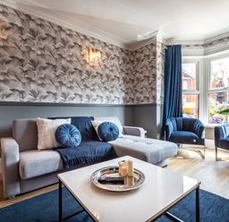 A living room with a grey sectional sofa and blue cushions blue armchairs and a white coffee table at Anchor House in Weymouth