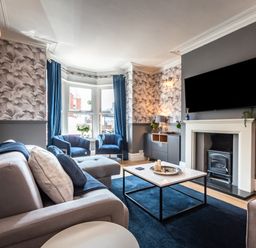 A living room with grey sofa blue chairs and a television above the fireplace at Anchor House in Weymouth