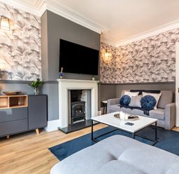 A living room with a grey sofa pillows a white coffee table a fireplace a TV wall cabinet and wooden floor at Anchor House in Weymouth
