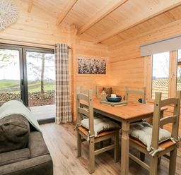 A dining area with a wooden table and chairs next to a sofa and large glass doors at Howgill Lodge in Gatebeck near Kirkby Lonsdale