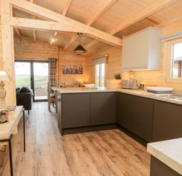 A kitchen with dark cabinets a sink and toaster next to a dining area with chairs and a table at Howgill Lodge in Gatebeck near Kirkby Lonsdale