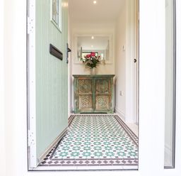 An entryway with a green door a patterned tile floor a distressed wooden cabinet with flowers and a mirror at Bluebell Cottage in Mary Tavy