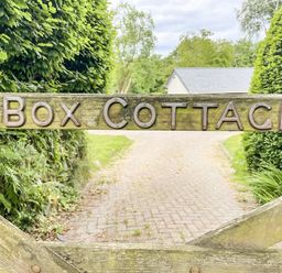 A wooden gate with Box Cottage sign with a paved driveway and greenery behind at Bluebell Cottage in Mary Tavy