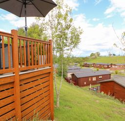 A wooden deck with umbrella overlooking several wooden cabins on a grassy hill at Rashierigg in Catterick North Yorkshire