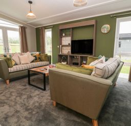 A living room with two sofas a coffee table a television on a stand and windows with curtains at Lily in Broadwoodwidger near Ashwater