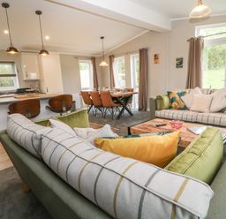 An open living room and kitchen area with sofas, cushions, a dining table with chairs, and pendant lights at Lily in Broadwoodwidger near Ashwater