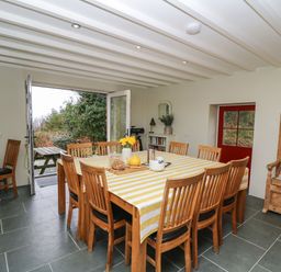 A dining room with a large table covered with a striped tablecloth surrounded by wooden chairs and an open door to a garden at Pen y Mynydd Newport Pembrokeshire