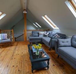 An attic living room with gray sofas a wooden chair a black glass coffee table with flowers and books wooden floors and skylight windows at Pen y Mynydd in Newport Pembrokeshire