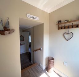 A hallway with wall decor including wooden sailboats and a heart hanging on a coat rack at May Bell Cottage in Dersingham