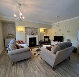 A living room with two sofas a fireplace a TV and a window at May Bell Cottage in Dersingham