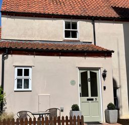Exterior of a small house with a green door marked number 5 two windows and a small fenced patio with table and chairs at May Bell Cottage in Dersingham