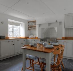 A kitchen with a wooden table set for four and white cabinets with wooden countertops at 12 Mill Green in Lyme Regis