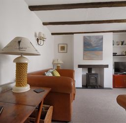 A living room with brown leather sofas wooden table lamps a wood burning stove and a TV on a cabinet at 12 Mill Green in Lyme Regis