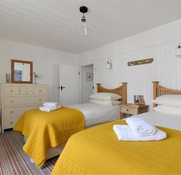 A bedroom with two single beds with yellow blankets and white towels a chest of drawers and a white armchair at 12 Mill Green in Lyme Regis