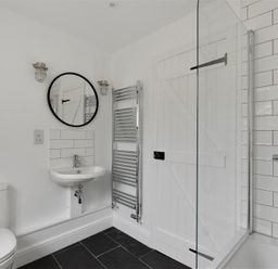 A bathroom with a toilet sink round mirror heated towel rail and a shower area at 12 Mill Green in Lyme Regis