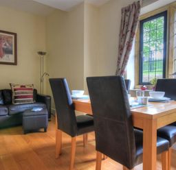 A dining area with a wooden table and four black chairs next to a window and a black leather sofa with cushions at Coram Lodge in Lyme Regis