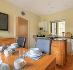 A kitchen with a wooden dining table set with cups bowls and glasses near an island and stainless steel oven at Coram Lodge in Lyme Regis