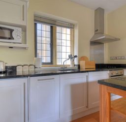 A kitchen with white cabinets a microwave toaster kettle utensils on the counter and a window at Coram Lodge Lyme Regis