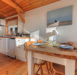 A kitchen with wooden ceiling and floor a dining table with plates and glasses and kitchen appliances at St Anton in Lyme Regis