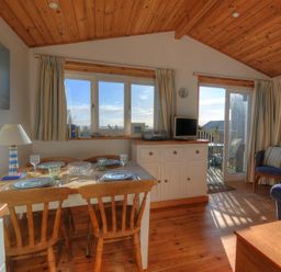 A dining table with chairs set for four near windows and a door leading to a balcony in a wooden ceiling room at St Anton in Lyme Regis
