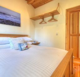 A bedroom with a wooden bed white bedding a wooden door and a wooden shelf with hangers at St Anton Lyme Regis