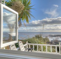 An open window overlooking a balcony with chairs and a view of the sea and boats at The Cabin in Lyme Regis