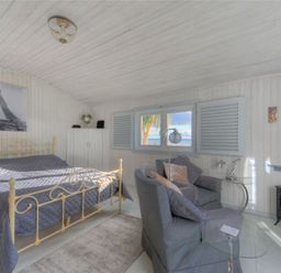 A bedroom with a metal bed, two armchairs, a window with shutters, and a small TV at The Cabin in Lyme Regis