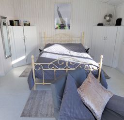A bedroom with a metal bed frame gray bedding two white wardrobes gray armchairs and a floor lamp at The Cabin in Lyme Regis