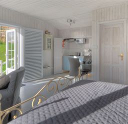 A bedroom with a bed a chair a small kitchen area a door and glass doors leading outside at The Cabin in Lyme Regis