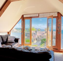 A living room with leather sofas facing a glass coffee table and large windows showing a seaside view at Bucket & Spade Lyme Regis