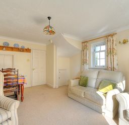A living room with a sofa, armchairs, a dining table with chairs, a bookshelf, and a window with curtains at Blacksmiths Cottage in Lyme Regis