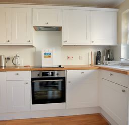 A kitchen with white cabinets wooden countertops an electric oven a kettle toaster and sink at Blacksmiths Cottage in Lyme Regis