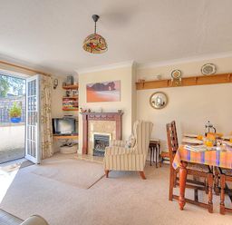 A living room with a fireplace armchair dining table and open door to outside at Blacksmiths Cottage Lyme Regis