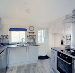 A kitchen with grey cabinets a stove a sink and a door at 1 Cobb View in Lyme Regis