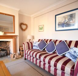 A living room with a striped sofa and cushions next to a fireplace with a wooden mantle at 1 Cobb View in Lyme Regis