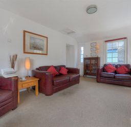 A living room with brown leather sofas red cushions wooden side tables lamps framed pictures and a wooden cabinet at Riverview in Lyme Regis
