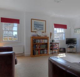 A living room with leather sofas bookshelf a television and windows with red blinds at Riverview Lyme Regis