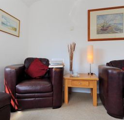 A living room with two brown leather armchairs with red cushions a wooden side table between them with a lamp and a vase and two framed pictures on the walls at Riverview in Lyme Regis