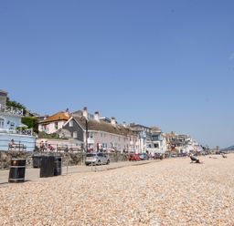 A pebble beach with people sitting on chairs and a row of houses along a promenade at 3 Argyle House in Lyme Regis
