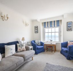 A living room with a grey sofa and blue armchairs near a window with striped blinds and a wooden table at 3 Argyle House in Lyme Regis